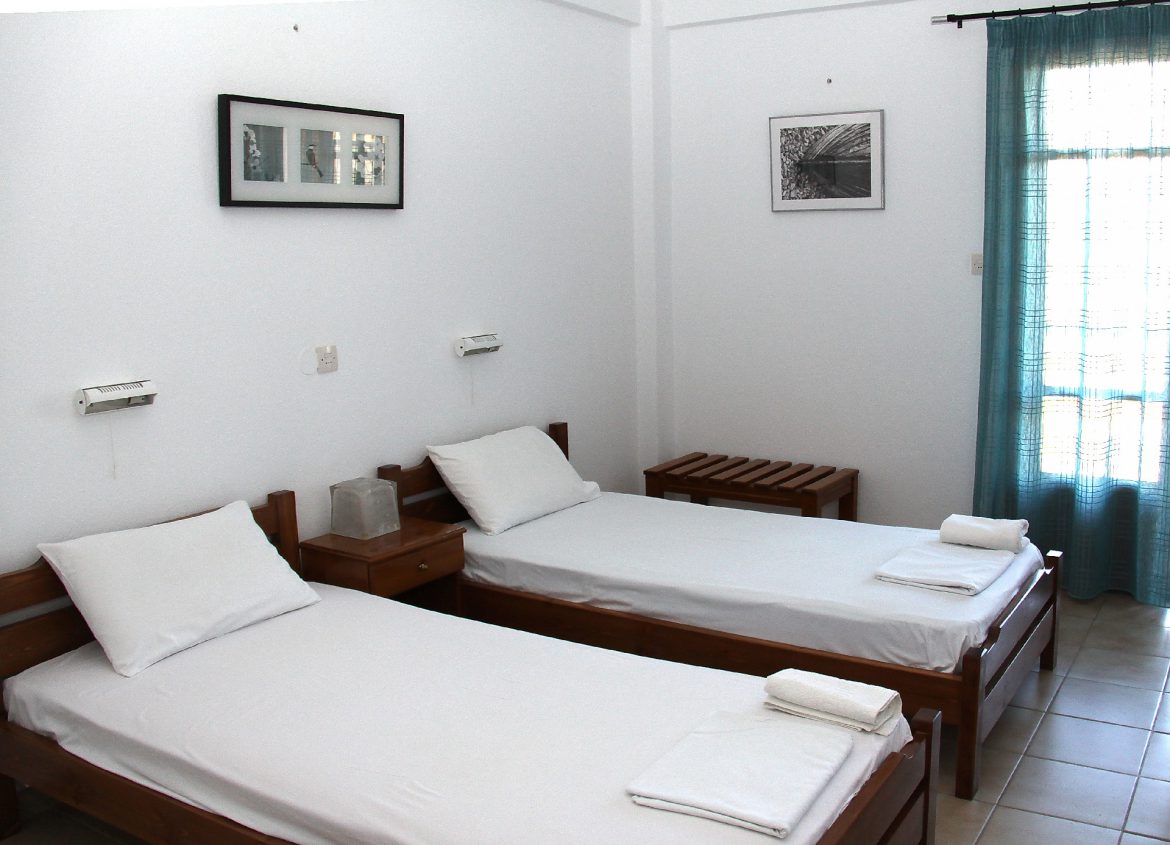 A triple room with three beds and a writing desk beside the balcony