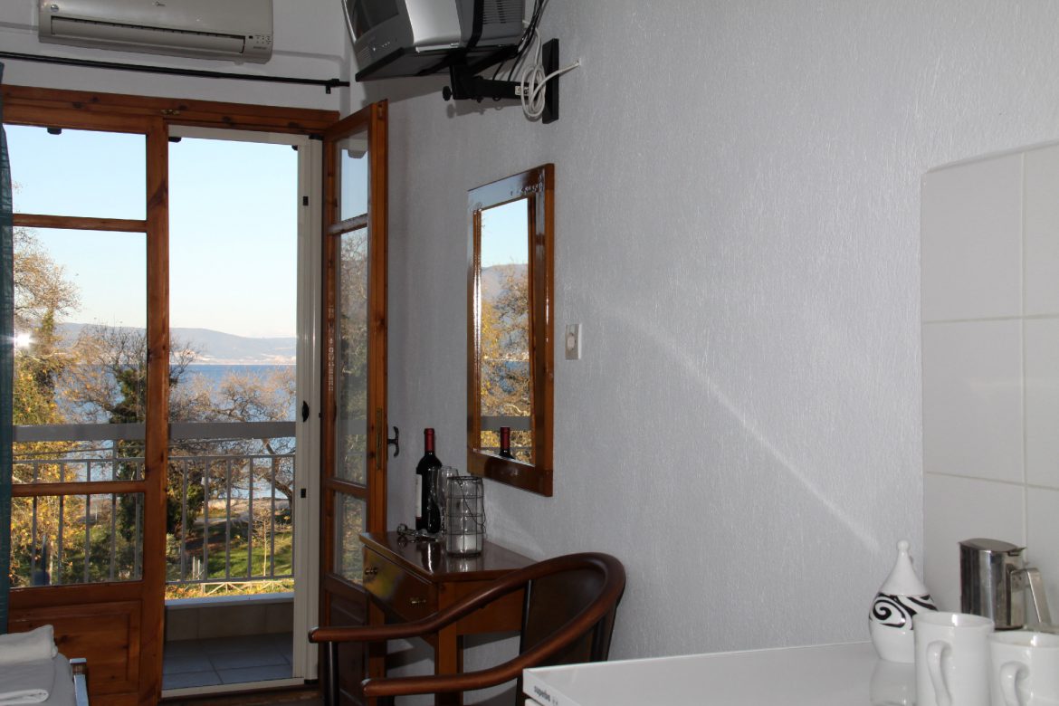 A room with the balcony door open onto the sea and the hills across the bay