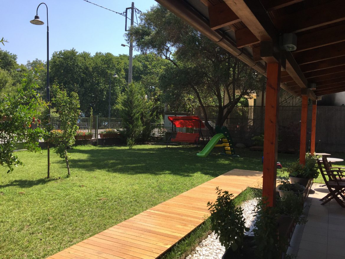 The hotel front garden with lawn, swing seat, children's slide and a wooden walkway