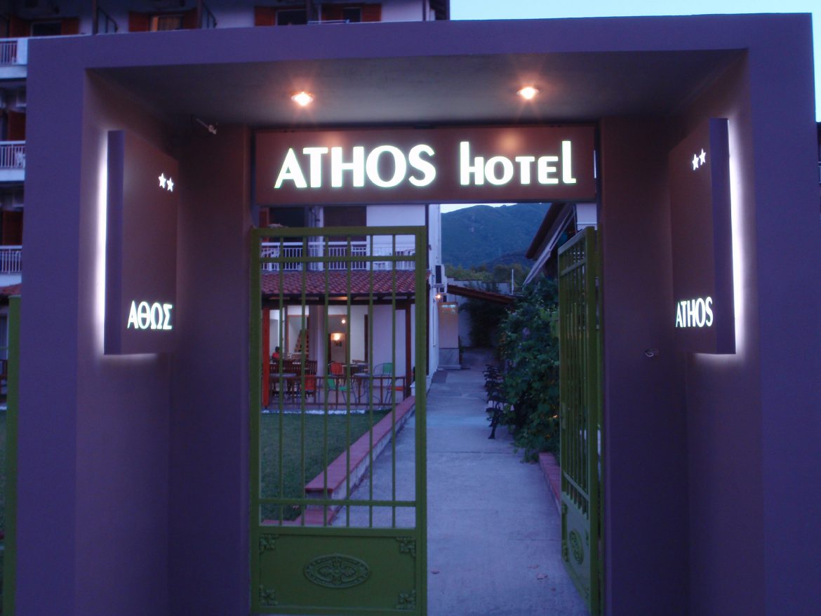 The lit Athos Hotel entrance arch and green gate at dusk